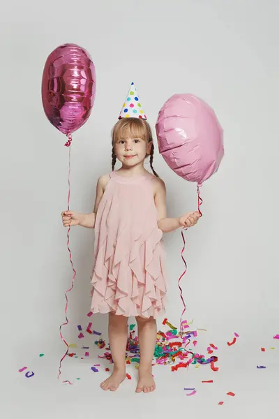 可爱的漂亮小女孩拿着两个粉色气球 背对着白色的工作室墙背景站着的时装肖像 带氦气气球的女童全长 生日派对概念 — 图库照片