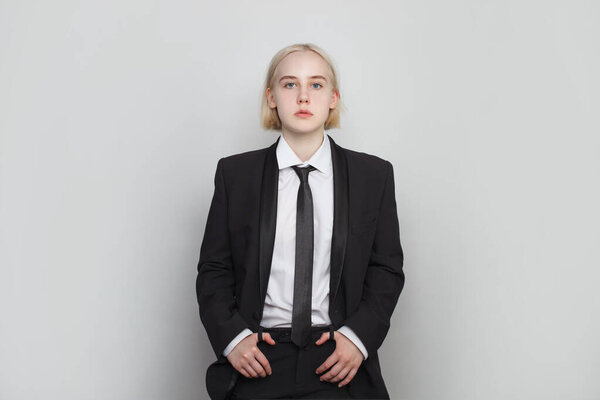 Portrait of a beautiful young business woman standing against grey background. Girl with short bob blonde hair wearing in suit and tie