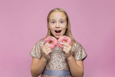 Şirin mutlu küçük kız parlak pembe stüdyo geçmişiyle donutla eğleniyor.