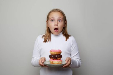 Gri arka planda pembe ve çikolatalı donutla beyaz tabak tutan şoke olmuş çocuk. Doğum günü partisi konsepti