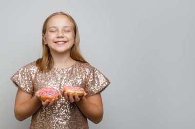 Beyaz arka planda iki tane pembe çörek tutan güzel küçük kız. Bir dilek tut. Doğum günü partisi konsepti