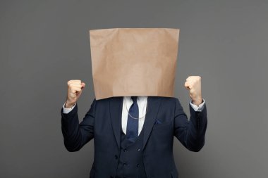 Kafasında boş kağıt torba olan iş adamı gri stüdyo duvarına karşı poz veriyor.