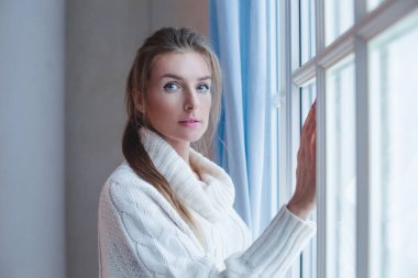 Beyaz süveterli, kapalı mekan portresi giyen neşeli genç bir kadın.