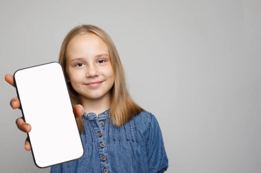 Güzel, neşeli küçük kız elinde boş beyaz ekran ekranlı akıllı telefon tutuyor.