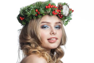 Dalgalı sarı saçlı, makyajlı ve beyaz arka planda yeşil kış çelengi olan mutlu genç model kadın. Güzel kadın yüzü. Yaklaş.