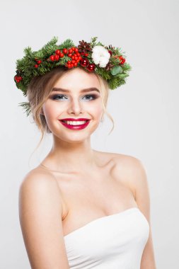 Şirin gülümseyen portresi olan güzel sarışın kadın. Sarışın, kıvırcık saçlı, makyajlı, yeşil ve kırmızı kış aksesuarlı, beyaz arka planda poz veren bir model.