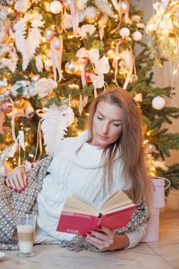 Evdeki Noel ağacının önünde kitapla dinlenen tatlı bir kadın.