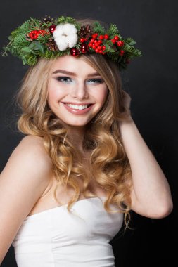 Uzun dalgalı saçları, makyajı ve siyah stüdyo arka planında renkli kış süslemeleri olan güzel model kadın, moda güzelliği portresi.