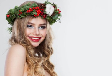 Uzun dalgalı saçları, makyajı ve beyaz stüdyo arka planında renkli kış süslemeleri olan gülümseyen model kadın, moda güzellik portresi.