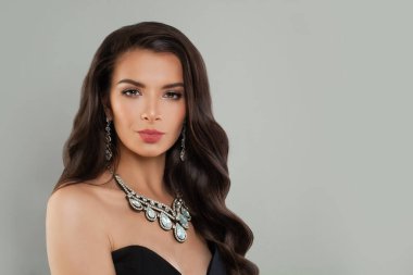 Mükemmel genç model kadın esmer, uzun kıvırcık saçlı, elmas küpeli, gri arka planda kolyesi olan, moda güzeli portresi olan.