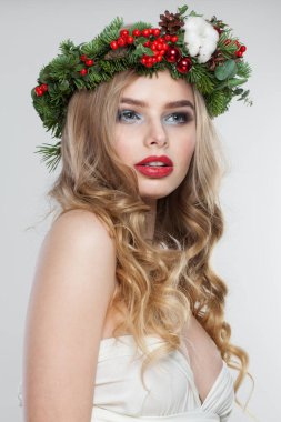 Şirin sarışın kadın portresi. Sarışın, kıvırcık saçlı, makyajlı, yeşil ve kırmızı kış aksesuarlı, beyaz arka planda poz veren bir model.