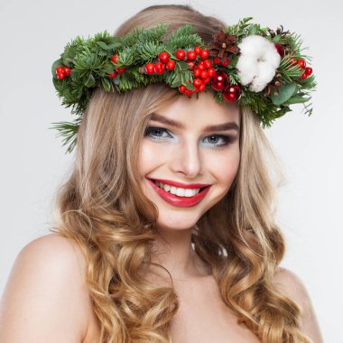 Gülümseyen sarışın kadın portresi. Sarışın, kıvırcık saçlı, makyajlı, yeşil ve kırmızı kış aksesuarlı, beyaz arka planda poz veren bir model.