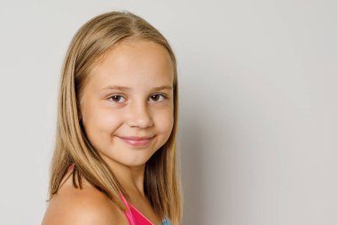 Neşeli genç kız, gri stüdyo arka planında kameraya bakıyor.