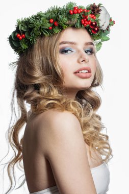 Parti makyajlı, uzun sarı kıvırcık saçlı ve beyaz arka planda Noel dekoru olan muhteşem sağlıklı genç bir kadın. Noel güzeli