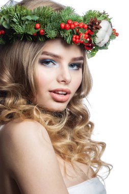 Parti makyajlı, uzun sarı kıvırcık saçlı ve beyaz arka planda Noel dekoru olan hoş, sağlıklı bir genç kadın. Noel güzeli