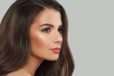 Gri arka planda uzun, siyah dalgalı saçları ve makyajı olan güzel bir kadın. Güzel yüz yakından, stüdyo portresi.