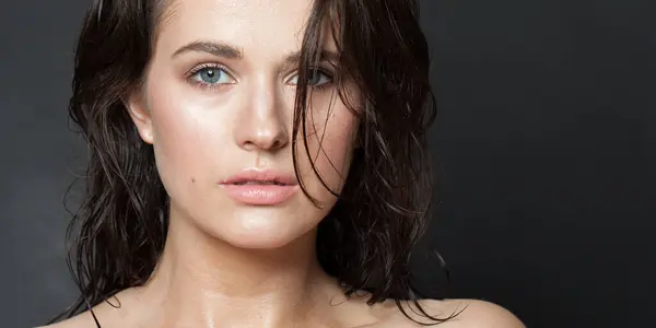 Beautiful woman with beauty face and healthy facial skin close up portrait. Beautiful wellness model with natural makeup and glowing hydrated skin on black background. Skin care