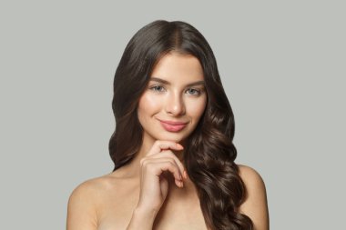 Uzun dalgalı saçlı, parlak tenli, beyaz arka planda poz veren neşeli esmer model kadın, moda güzellik stüdyosu portresi.