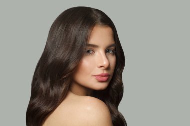 Çekici esmer moda güzellik portresi. Gri stüdyo arka planında uzun, siyah, sağlıklı saçları ve taze cildi olan genç model bir kadın.