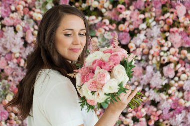 Şirin gülüşlü, elinde çiçek hediyesi olan ve pembe çiçekli arka planda poz veren romantik, mutlu esmer kadın. Çiçek açan, aşkım, 8 Mart doğum günü tatili konsepti