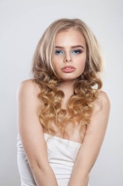 Beyaz arka planda izole edilmiş, şehvetli, sağlıklı sarışın bir model. Makyajlı, temiz tenli ve dalgalı sarı saçlı bir kadın. 