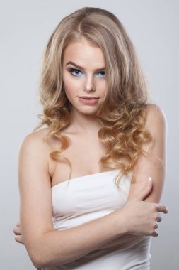 Beyaz arka planda izole edilmiş genç, sağlıklı bir sarışın model. Makyajlı, temiz tenli ve dalgalı sarı saçlı bir kadın. 