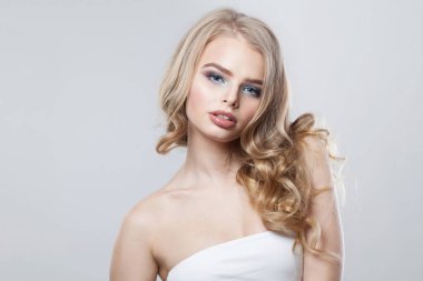 Temiz ve uzun kıvırcık saçlı zarif genç bir kadın beyaz stüdyo arka planındaki kameraya bakıyor.