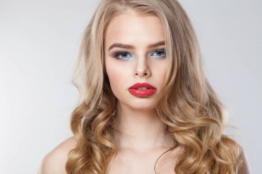 Temiz tenli, uzun kıvırcık saçlı, beyaz stüdyo arka planındaki kameraya bakan şık bir genç kadın.