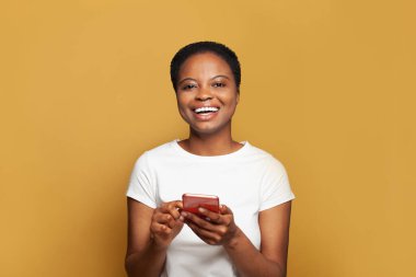 Gülen genç bir kadın telefonunda mesaj atıyor. Akıllı telefon kullanan, mesajlaşan ya da sosyal ağları tarayan mutlu model öğrenci