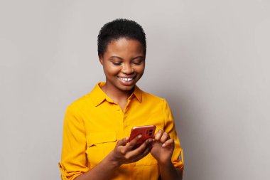 Telefonunda mesaj atan gülümseyen genç bir kadın. Akıllı telefon kullanan, mesajlaşan ya da sosyal ağları tarayan mutlu model öğrenci