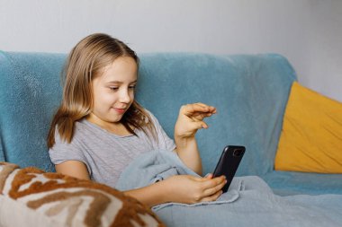 Boş zaman, çocuklar, teknoloji, internet iletişimi ve insanlar konsepti. Akıllı telefonlu gülümseyen kız mesaj atıyor, video izliyor ya da evde oyun oynuyor.