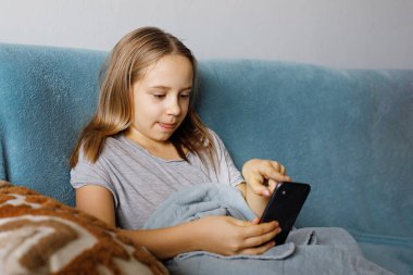 Komik meraklı kız evde akıllı telefon kullanıyor. Rekabetçi bir video oyununda oynayan ya da akıllı telefondan sohbet eden şirin bir çocuğun portresi 