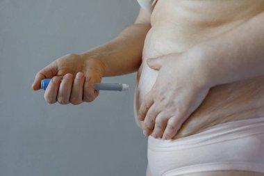 Semaglutid mavi enjeksiyon kalemi ve kadın vücudu gri arka plana yakın çekim. Kan şekerini ve kilo kaybını iyileştirmek için kullanılan semaglutid hormonu. 