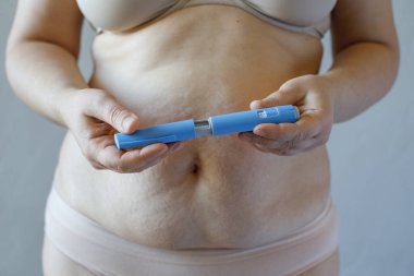 Mavi Semaglutide enjeksiyon kalemi yakın plan. Kadın karnına karşı semaglutid ya da insülin ilacı. Semaglutide, Diyabet ve Kilo Verme kavramı. 