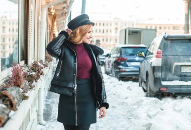 Kar şehrinin caddesinde duran siyah deri ceketli mutlu, büyüleyici esmer kadın.