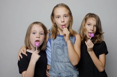 Mutlu çocuklar beyaz stüdyo duvarında lolipop şekeri yiyorlar. Arka plan, moda portresi.  