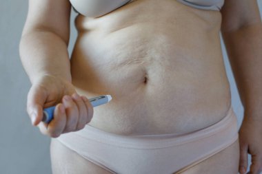 Semaglutid enjeksiyonu. Semaglutid veya insülin enjeksiyon kalemi ve kadın vücudu arka planda gri duvara yakın çekim yapar. Kan şekerini ve kilo kaybını iyileştirmek için kullanılan semaglutid hormonu. 