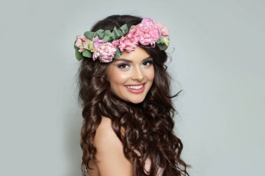 Makyajlı güzel bir kadın, kusursuz beyaz dişli gülüşü ve bahar veya yaz mevsimi çiçekli çelengi uzun parlak dalgalı saçları, moda stüdyosu portresi 