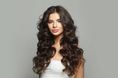 Genç, sağlıklı, esmer, uzun, koyu renk saç stili ve gri arka planda taze cildi olan bir kadın. Moda güzellik portresi. Saç bakım, saç şekillendirme ve şampuan konsepti