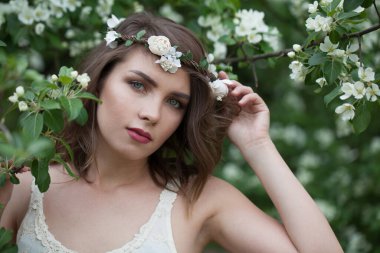 Sağlıklı, genç, yetişkin bir kadın model. Temiz ciltli, makyajlı ve yeşil yapraklı arka plan portresi üzerinde çiçek bahçesinde kahverengi saçlı.