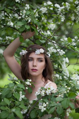 Açık tenli, makyajlı, yeşil yapraklı arka plan portresi üzerinde çiçek bahçesinde kahverengi saçlı muhteşem, genç bir kadın model.