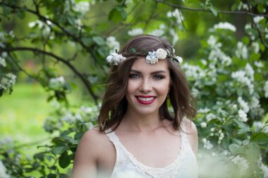 Makyajlı güzel bir kadın model, temiz bir ten, sağlıklı saç stili ve çiçek parkında samimi bir gülümseme. Doğal güzel kadın portresi.