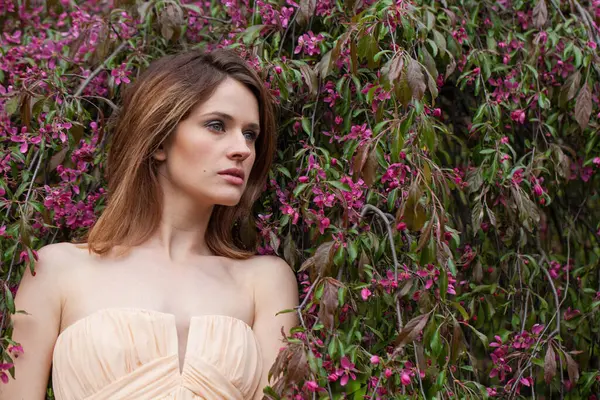 stock image Glorious young adult brunette female model with fresh clean skin, bob haircut and natural makeup against green blurred leaves background with white spring flower