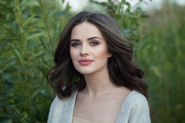 Makyajlı, temiz tenli, sağlıklı saç stili olan ve çiçek parkında gülümseyen hoş bir bayan model. Doğal güzel kadın portresi.