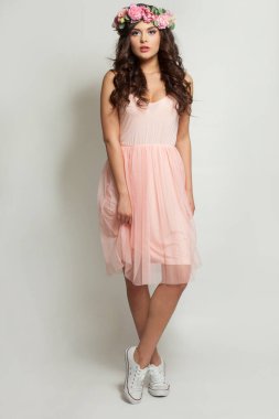 Pembe elbiseli, beyaz ayaklı, güzel bir manken kadın beyaz stüdyo arka planında duruyor.