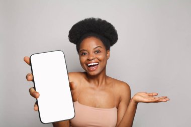 Gri stüdyo arka planında beyaz boş ekran ekranı olan akıllı telefonu tutan mükemmel sağlıklı bir kadın. Telefonlu mutlu model