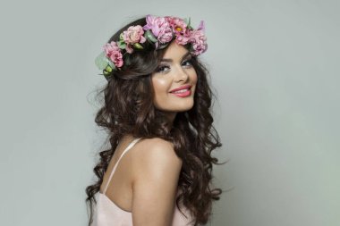 Beyaz arka planda kameraya bakan uzun dalgalı saçlı, makyajlı ve tatlı gülüşlü esmer kadın model.