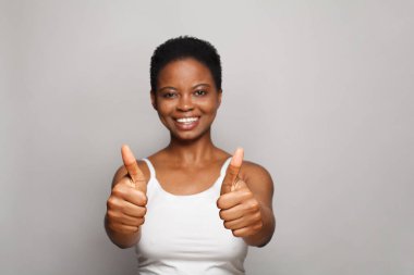 Gülümseyen neşeli kadın beyaz arka planda baş parmağını gösteriyor.