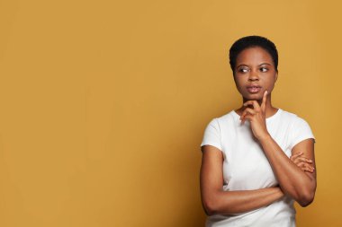 Beyaz tişörtlü Afro-Amerikan kadının renkli sarı arka planda durması çok hoş.