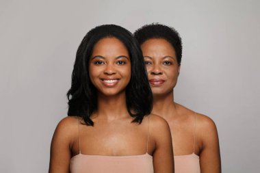 Gri arka planda gülümseyen genç ve olgun bir kadın. Yaşlanma, kozmetoloji, estetik ameliyat ve konsept öncesi ve sonrası rötuş